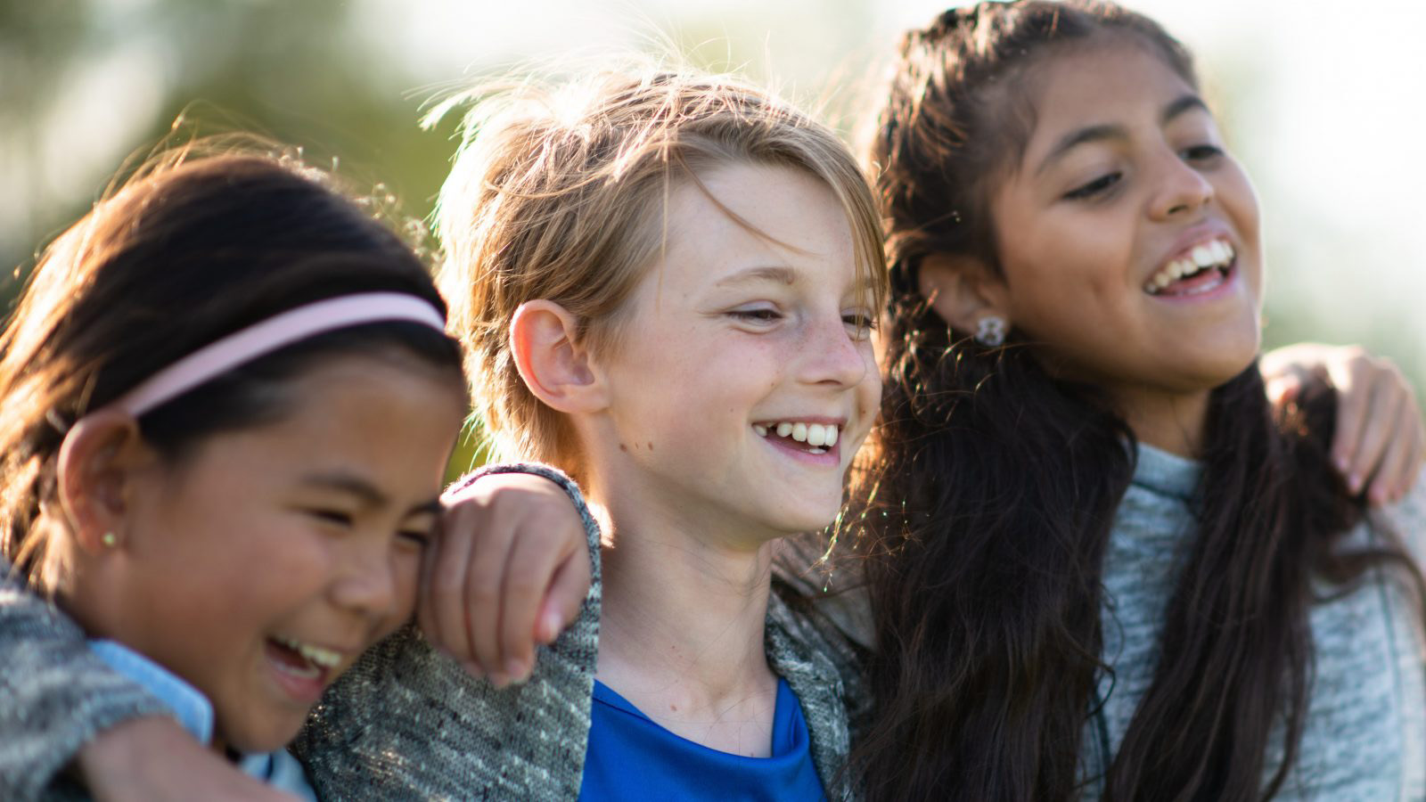 Tre børn holder hinanden om skuldrene og griner
