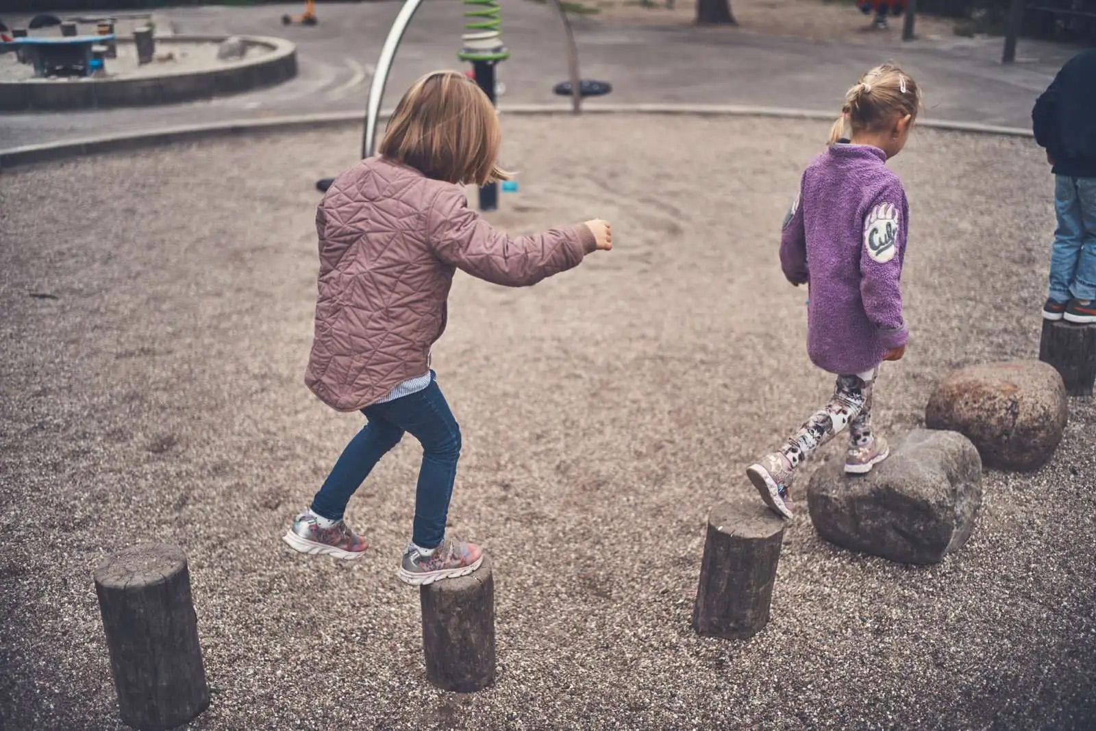 To piger går på stammer og sten lagt ud på en legeplads