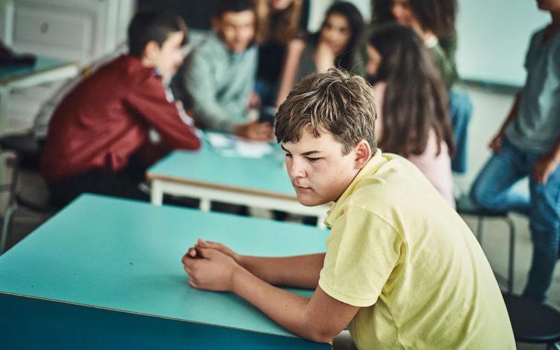 Dreng i gul trøje sidder alene uden for fællesskabet