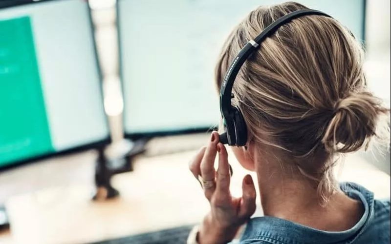 Kvinde med headset sidder foran to skærme