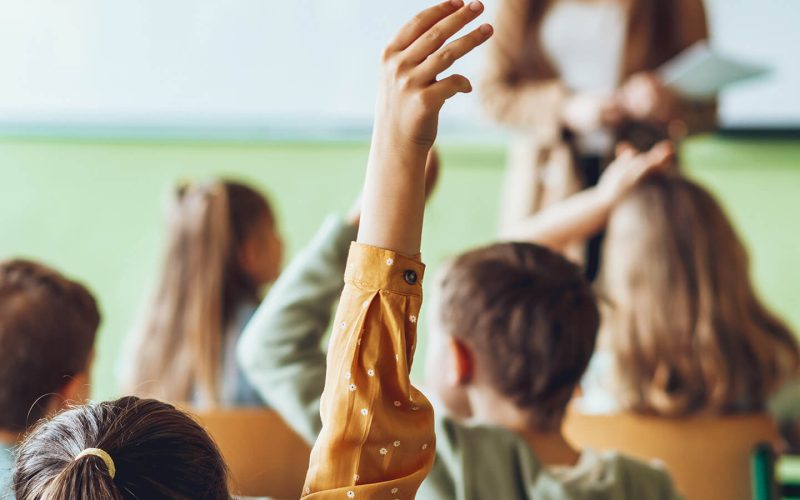 Børn i klasselokale med hænderne i vejret