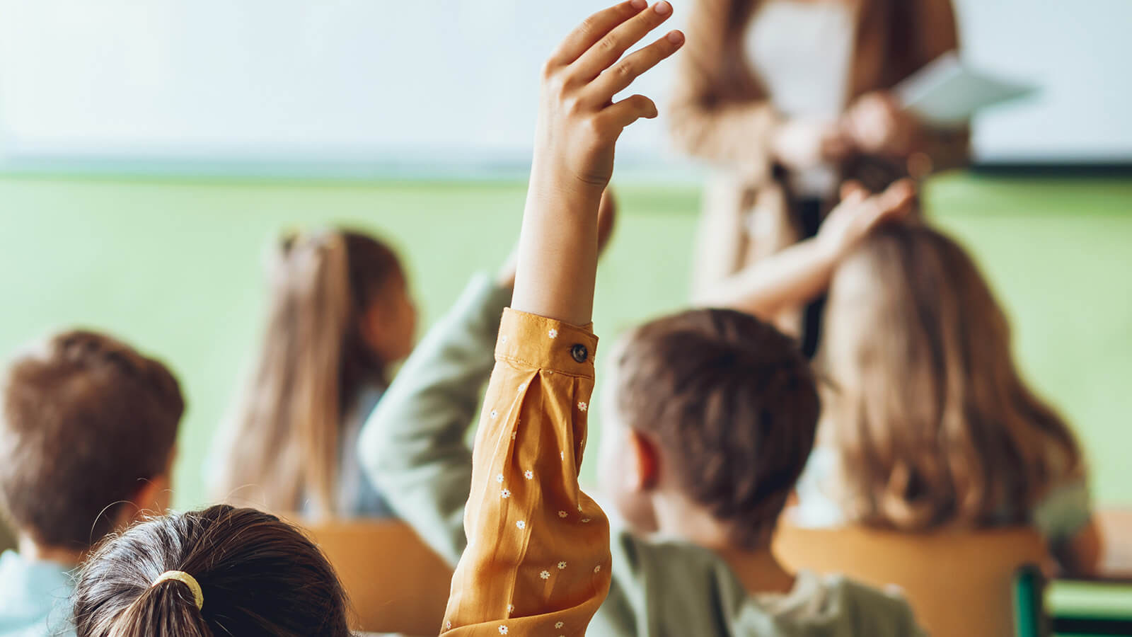 Børn i klasselokale med hænderne i vejret