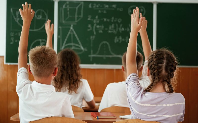 Børn i klasselokale med hænderne i vejret