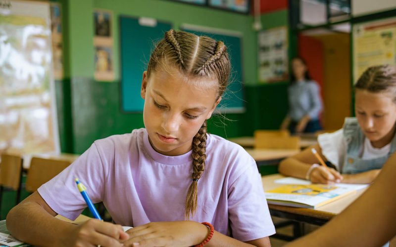 Pige sidder i klasselokale og skriver