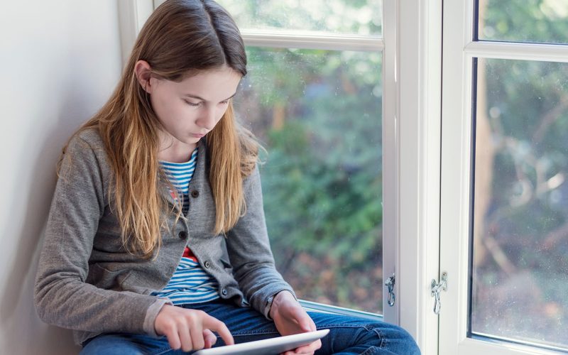 Pige sidder i vindueskarm med en tablet
