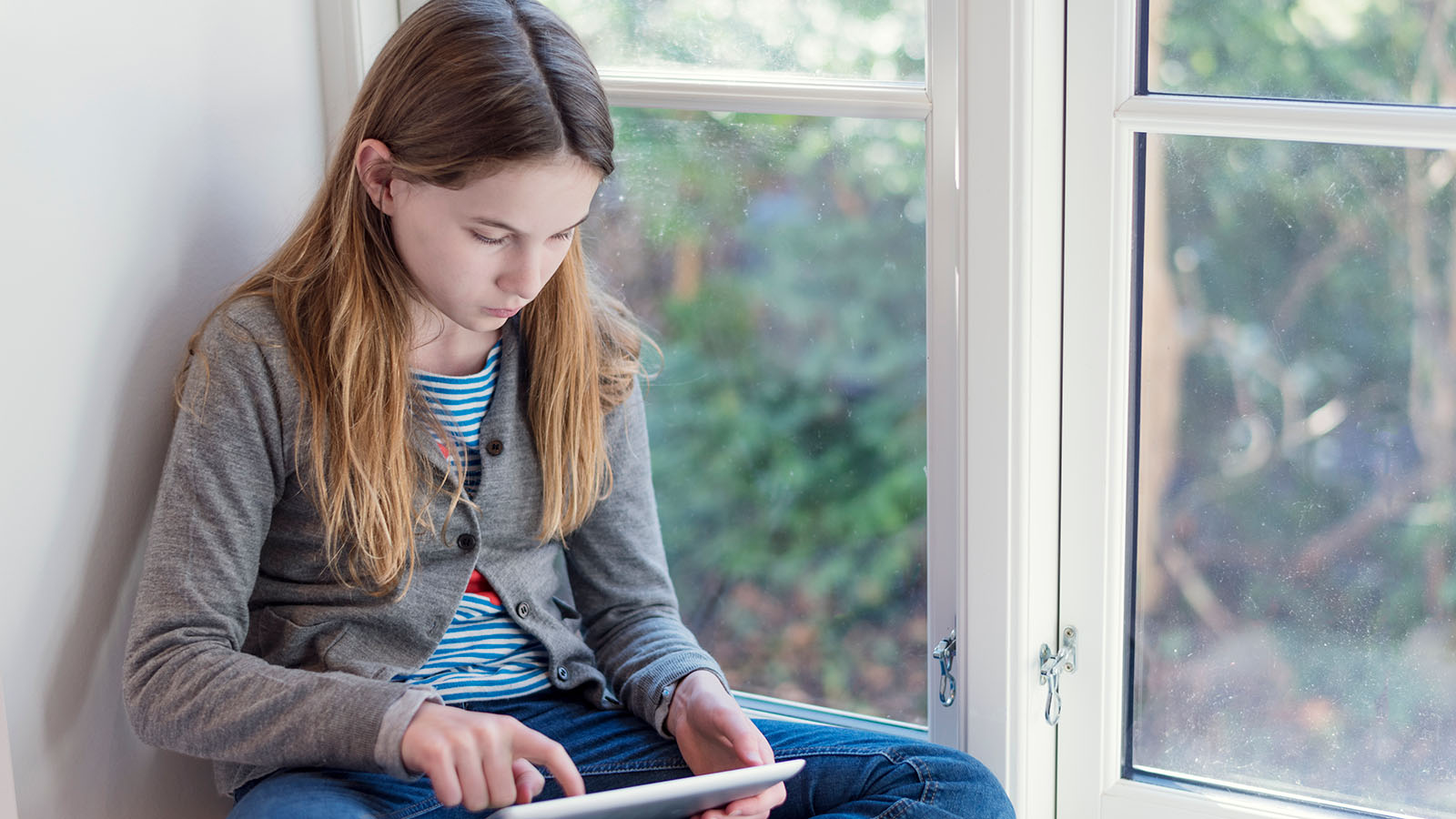 Pige sidder i vindueskarm med en tablet