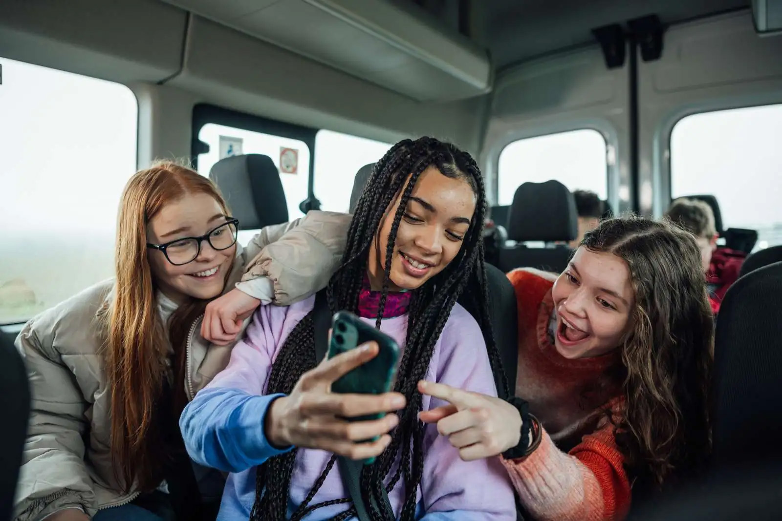 Tre piger sidder i en bus og kigger på en mobil