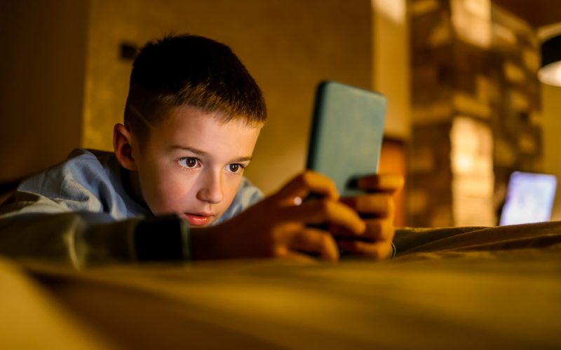 Dreng der ligger på en seng og kigger på sin telefon®é