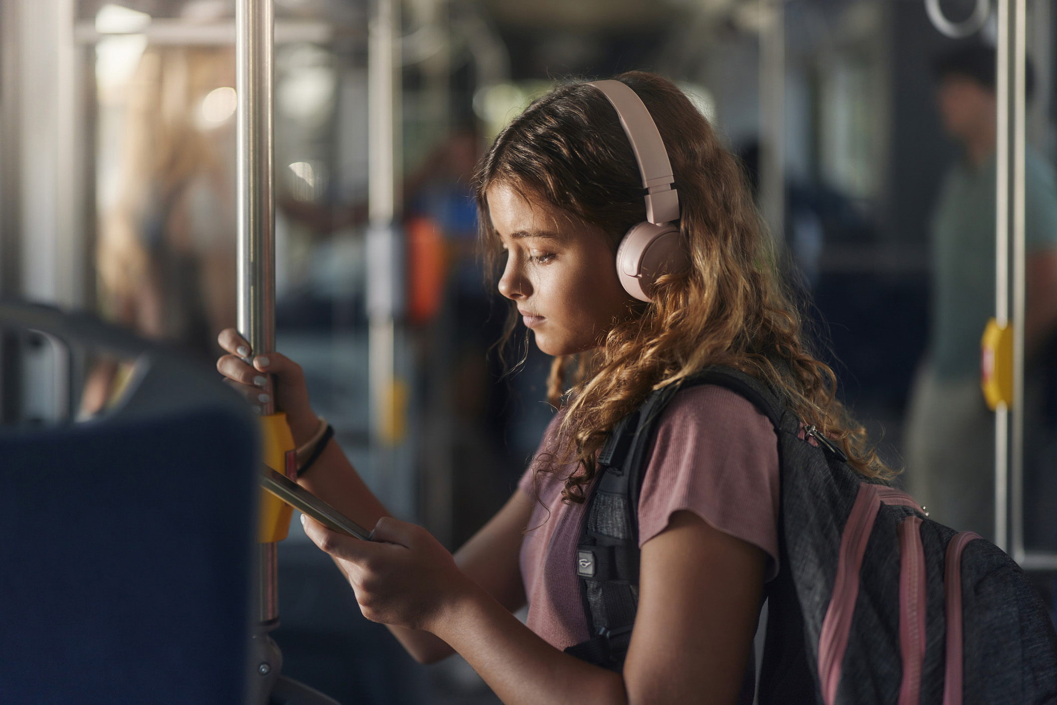 Pige står med høretelefoner på i en bus og kigger på sin mobil